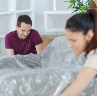 2 people moving sofa covered in plastic furniture wrap